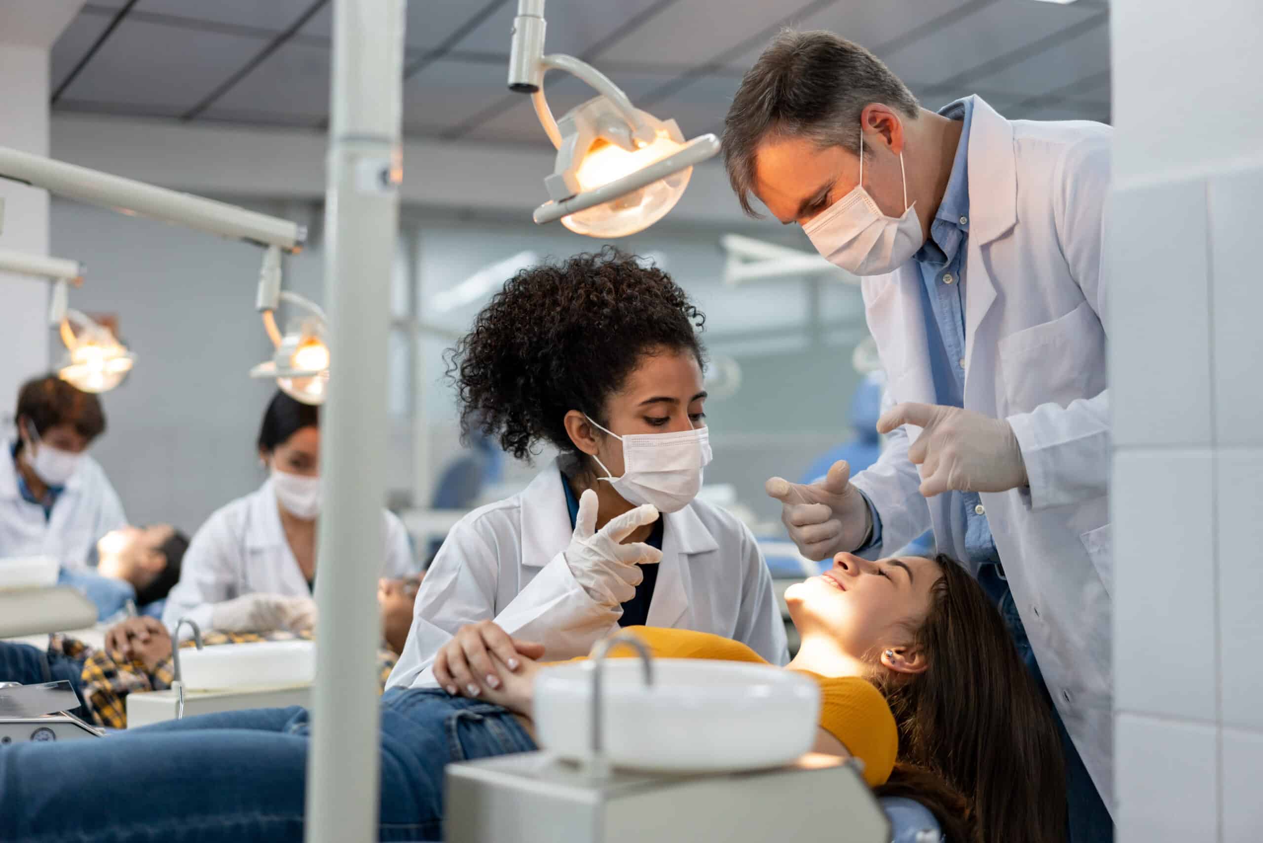 Dentist and dental assistant consult with patient laying in examination chair.