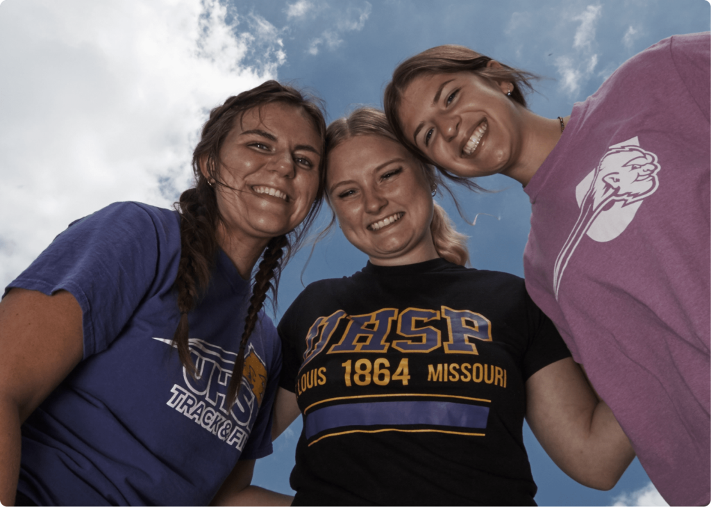 Three undergraduate female students posing with sunny skies in the background