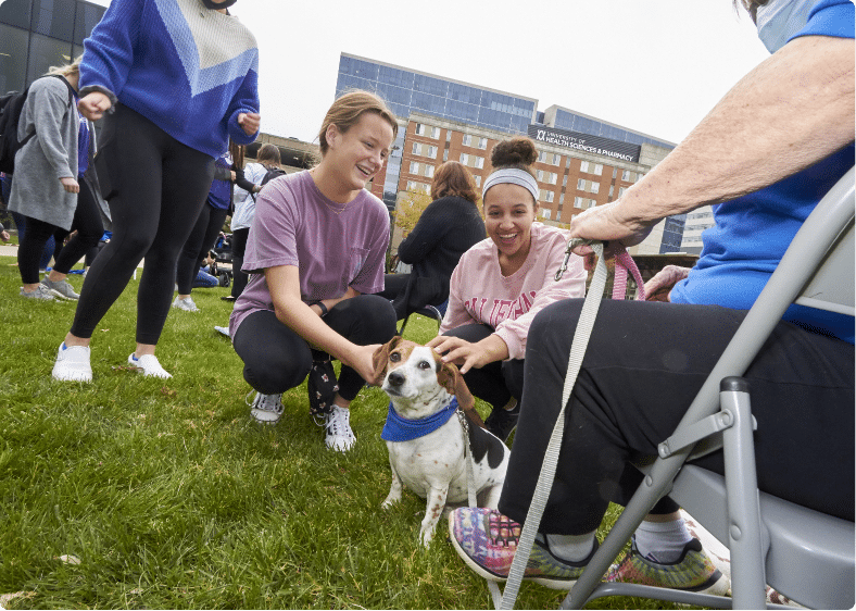 Happy students pet a puppy during at event outside on campus.