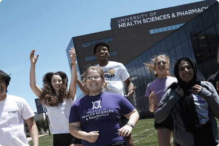 Group of five students jumping and smiling in front of UHSP building