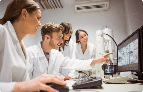 Group of four students wearing medical robes looking at imaging on a computer screen