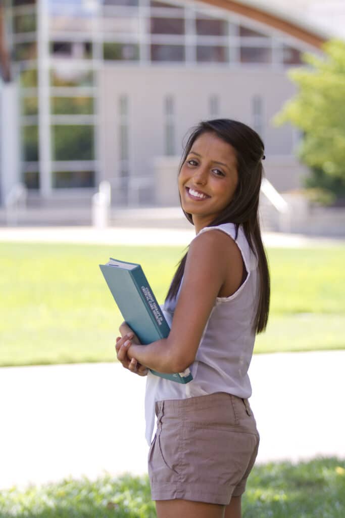 Alumna Sonalie Patel stands in the quad holding books and looking over her shoulder