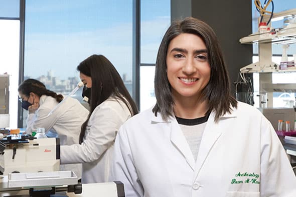 Ream Al-Hasani smiles in her lab in the Center for Clinical Pharmacology with team researchers working in the background.