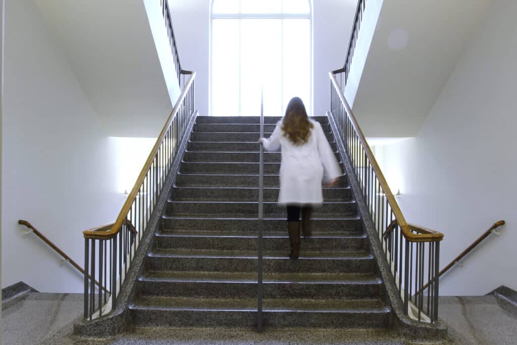 student in white coat walks up stairs in Jones Hall