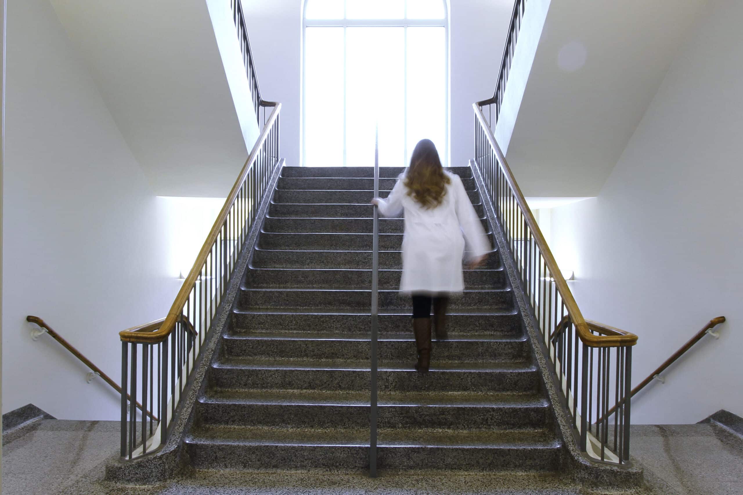 A student in a white coat walking up a staircase in Jones Hall