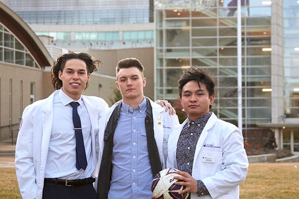 Students Edward Ngo, Sean Harris, and Brent Adams posing in their white coats on the quad