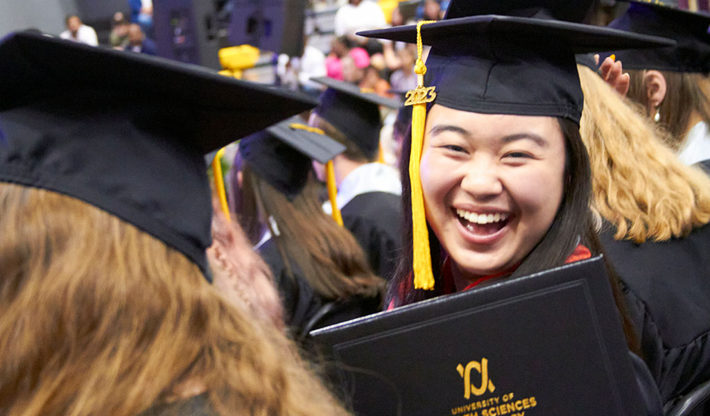 Student smiles holding diploma during the College of Arts and Sciences commencement ceremony.