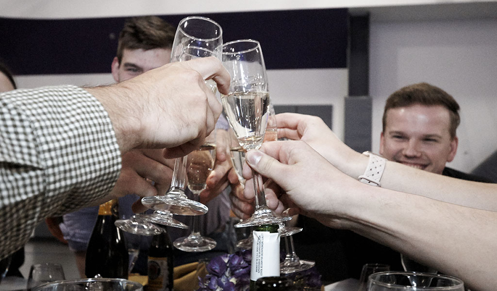 Circle of guest cheers champagne glasses during grad happy hour event.