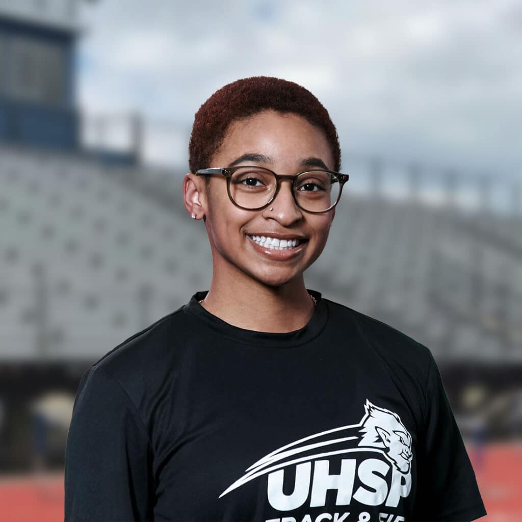 UHSP student-athlete Taylor Washington smiles on the running track in front of bleachers