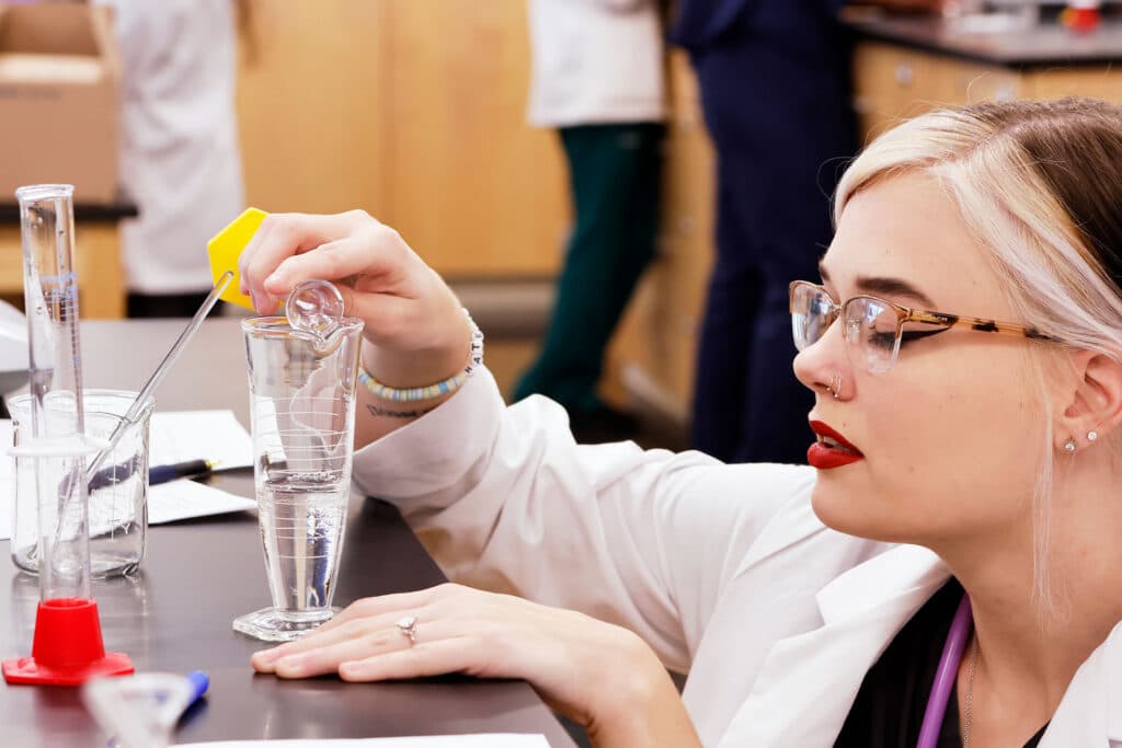 pharmacy student pours liquid into vessel at eye level