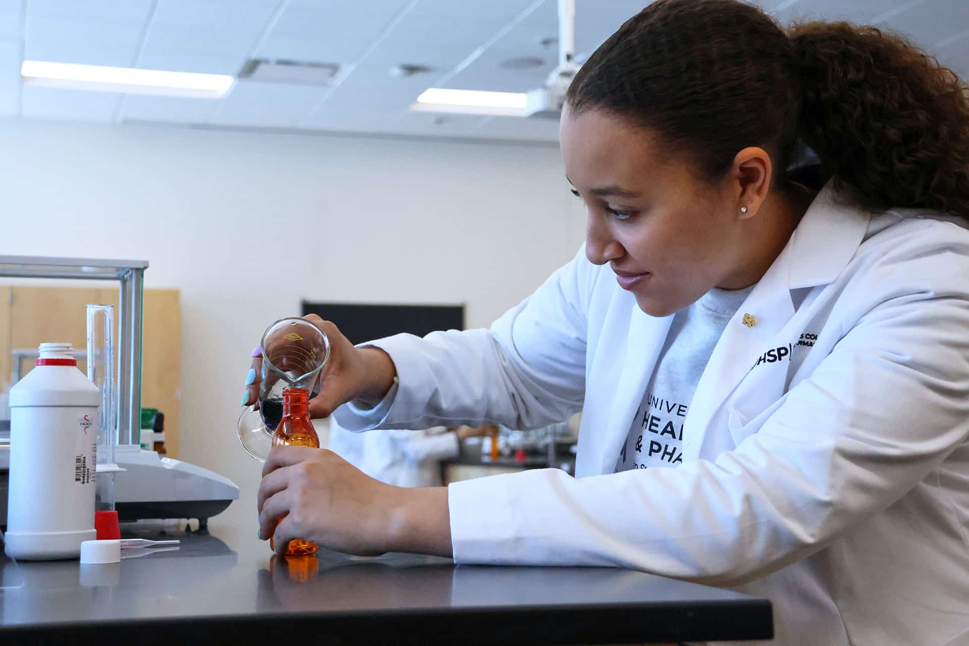 pharmacy student pours medication into vessel