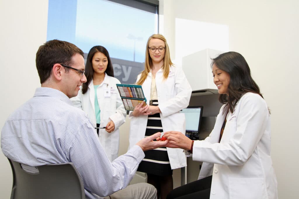 student pharmacist examines a patient in an exam room while faculty preceptor observes